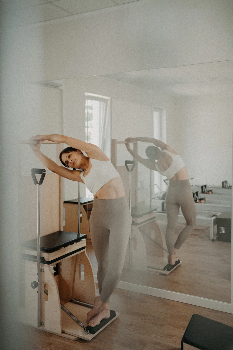 Instruktorka pilates w bocznym rozciągnięciu przy electric chair w jasnej sali Holica Studio